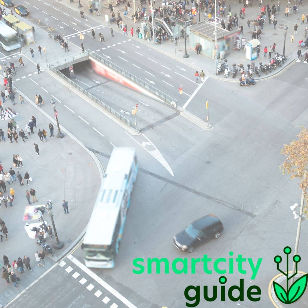 Luftaufnahme einer belebten Stadtkreuzung mit fahrenden Bussen und Autos, Menschen und dem Logo Smart City Guide.